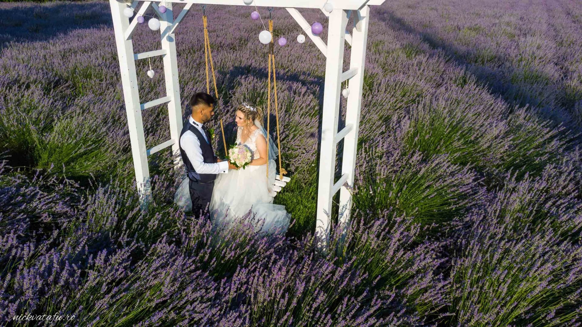 Mire și mireasă pe o leagănă în câmpul de lavandă, emoție pură într-o fotografie de nuntă romantică.