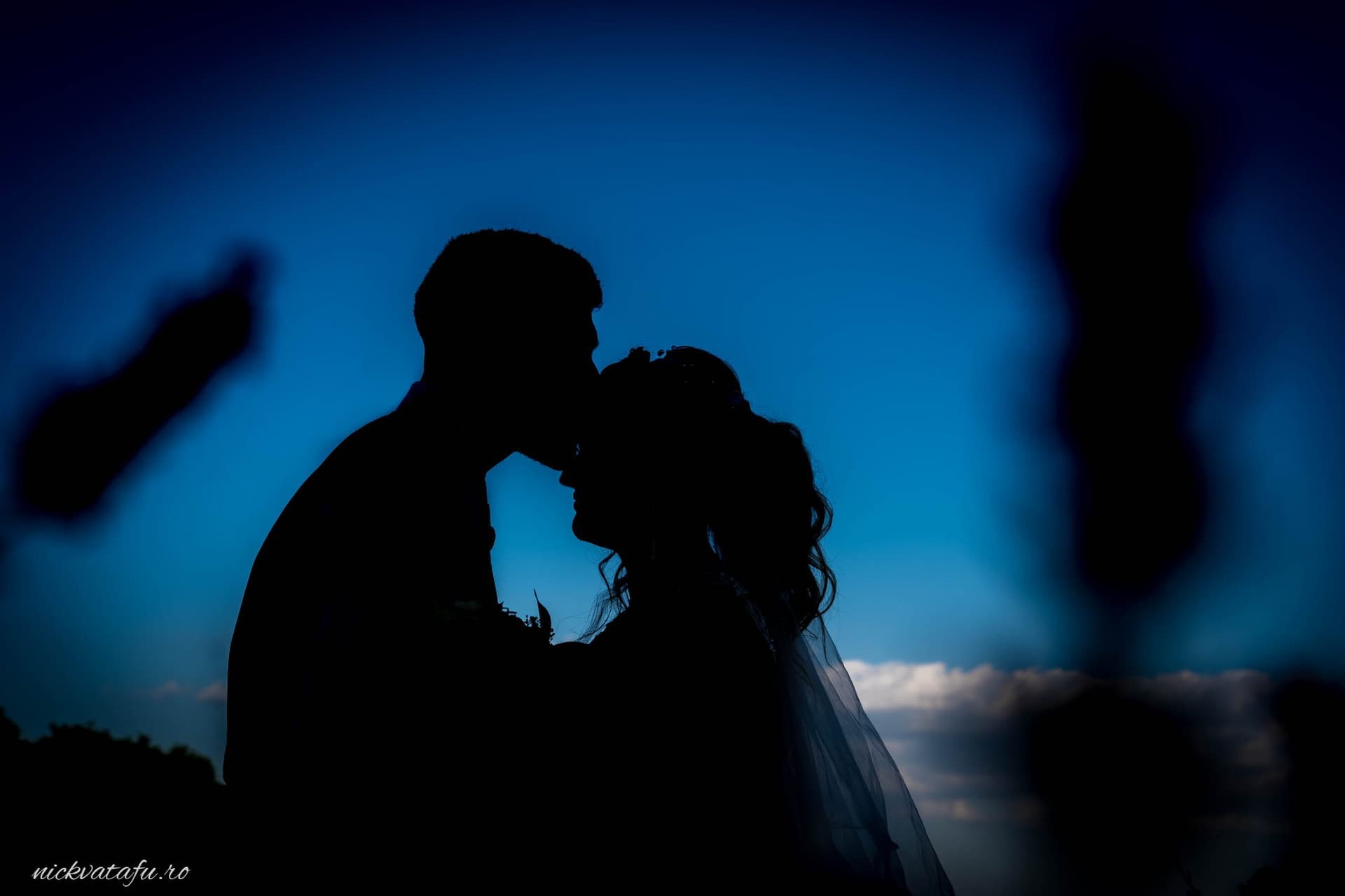 Mire și mireasă în umbra unei îmbrățișări pline de emoție, sub cerul albastru, fotografie de nuntă romantică.