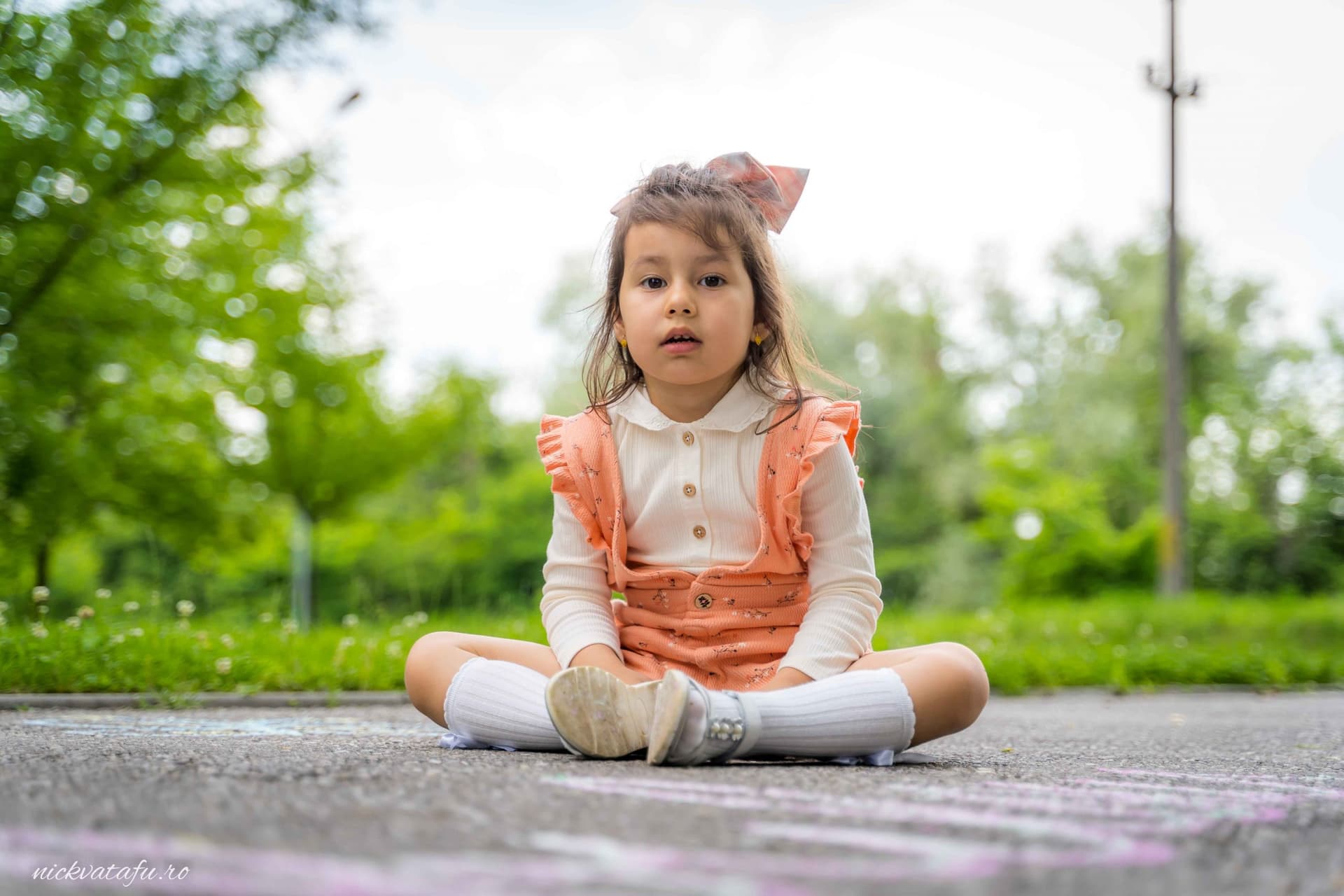 Fetiță îmbrăcată elegant, stând pe asfalt, cu o expresie curioasă, într-o atmosferă relaxantă de natură.