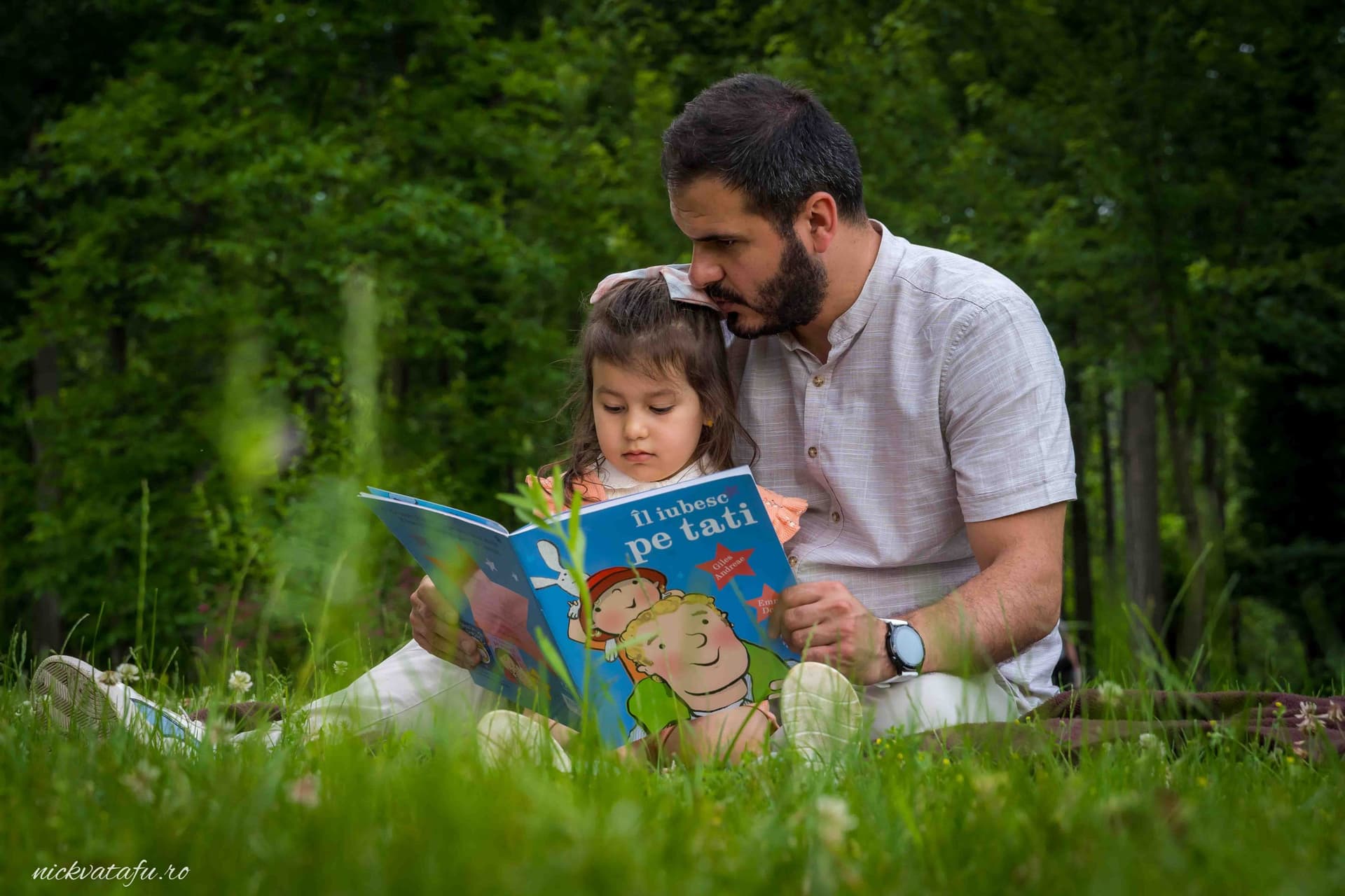 Părinte și copil citind o carte în natură, moment plin de emoție și intimitate.