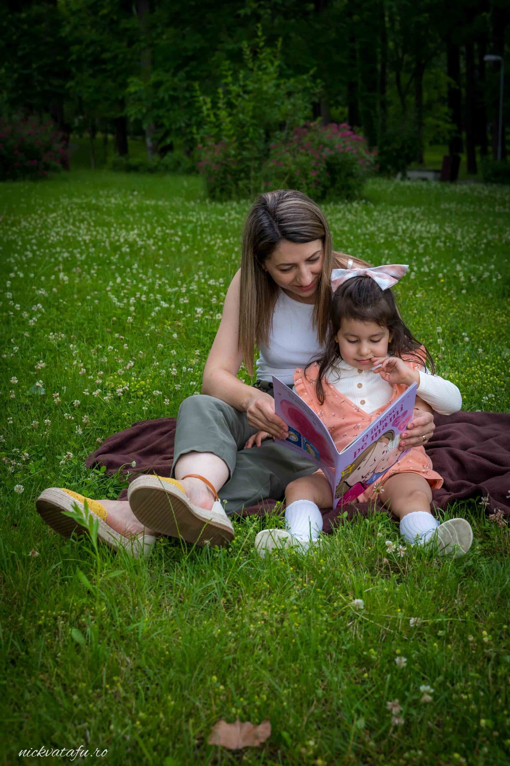 Mamă și fiică citind împreună pe iarbă, surprinse într-un moment plin de emoție și intimitate.