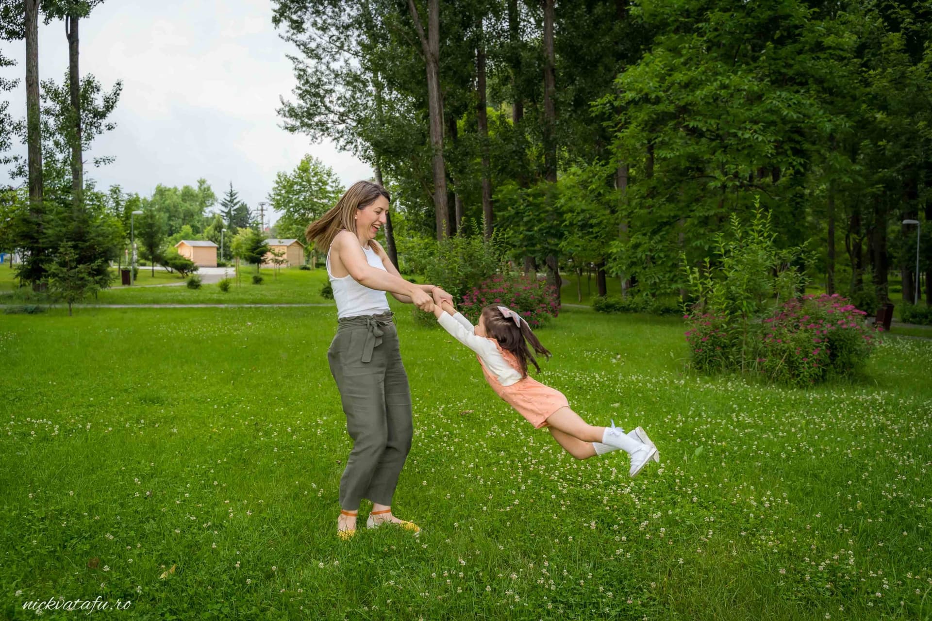 Femeie zâmbitoare se joacă cu o fetiță în natură, evocând emoție și bucurie, perfect pentru o fotografie de familie.