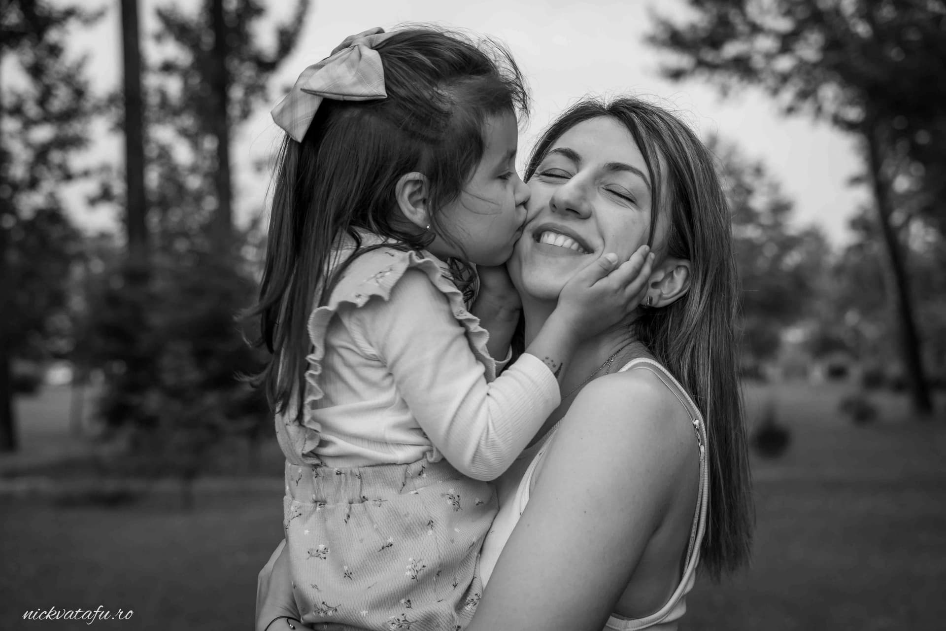 Fetiță îmbrățișându-și mama cu un sărut jucăuș, capturând emoția și bucuria unui moment special.