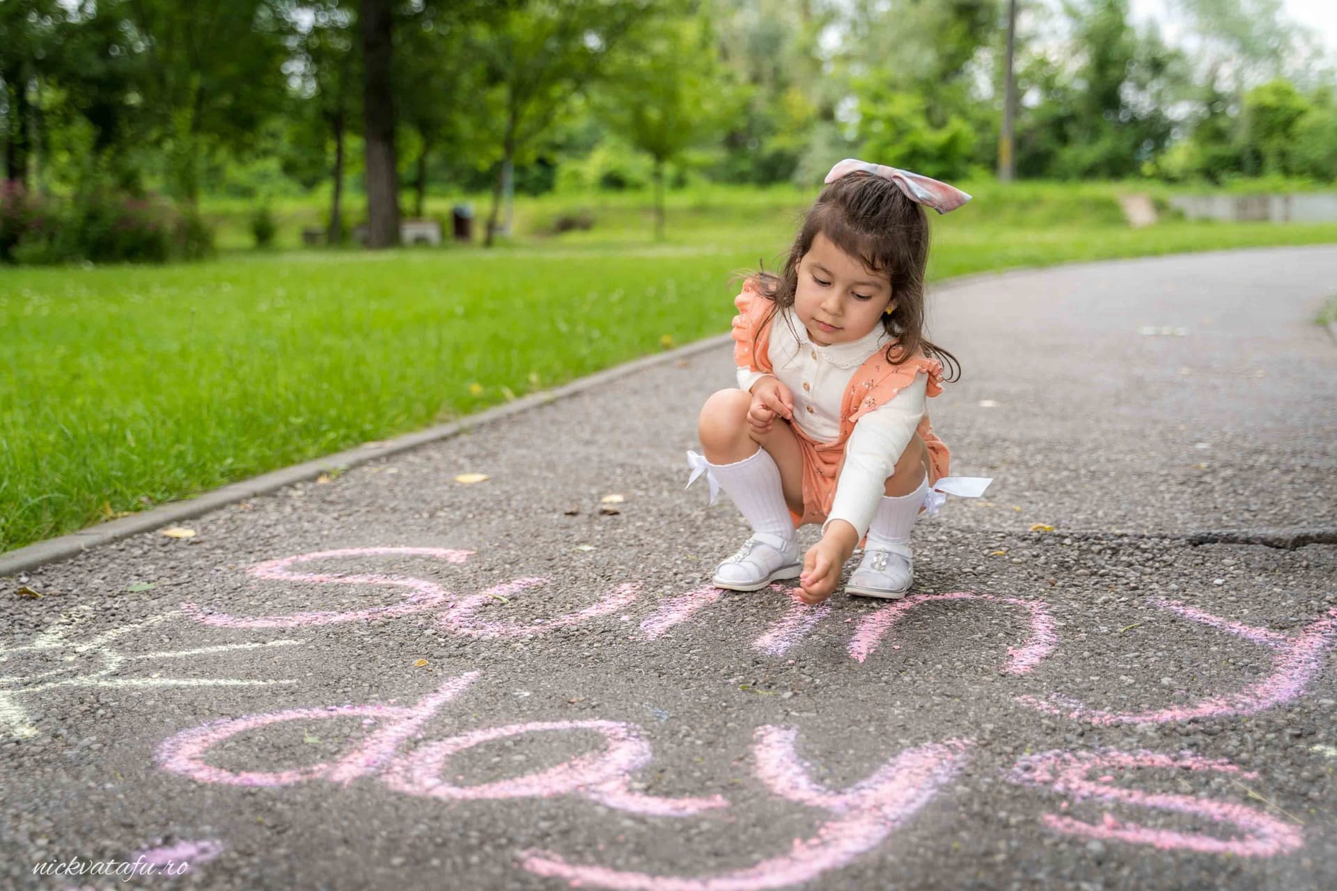 Fetiță jucându-se cu cretă pe asfalt, scriind un mesaj vesel într-un parc, plin de emoție și bucurie.