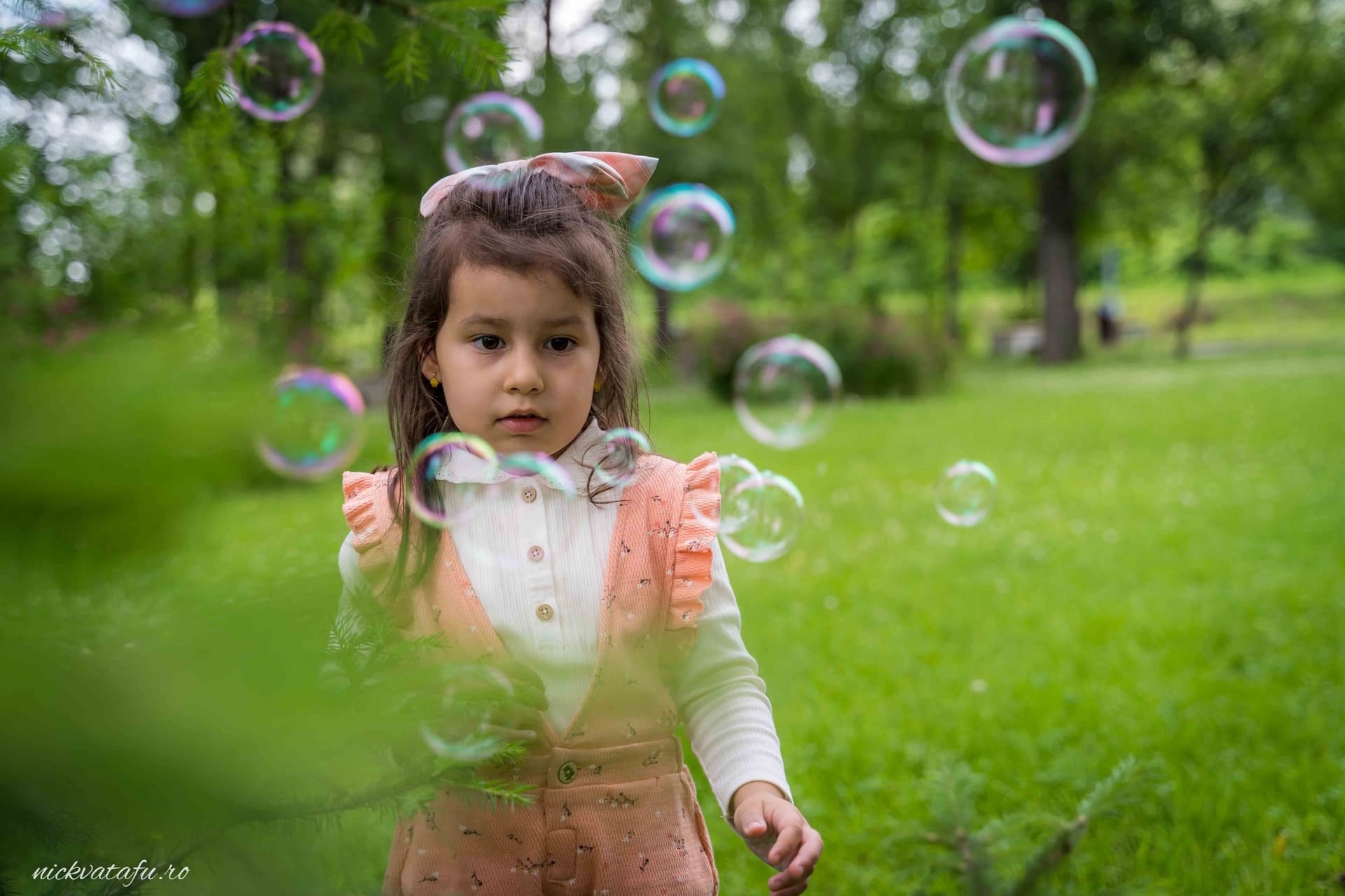Fetiță jucându-se cu bule de săpun într-un parc verde, capturând emoția inocenței și bucuriei.