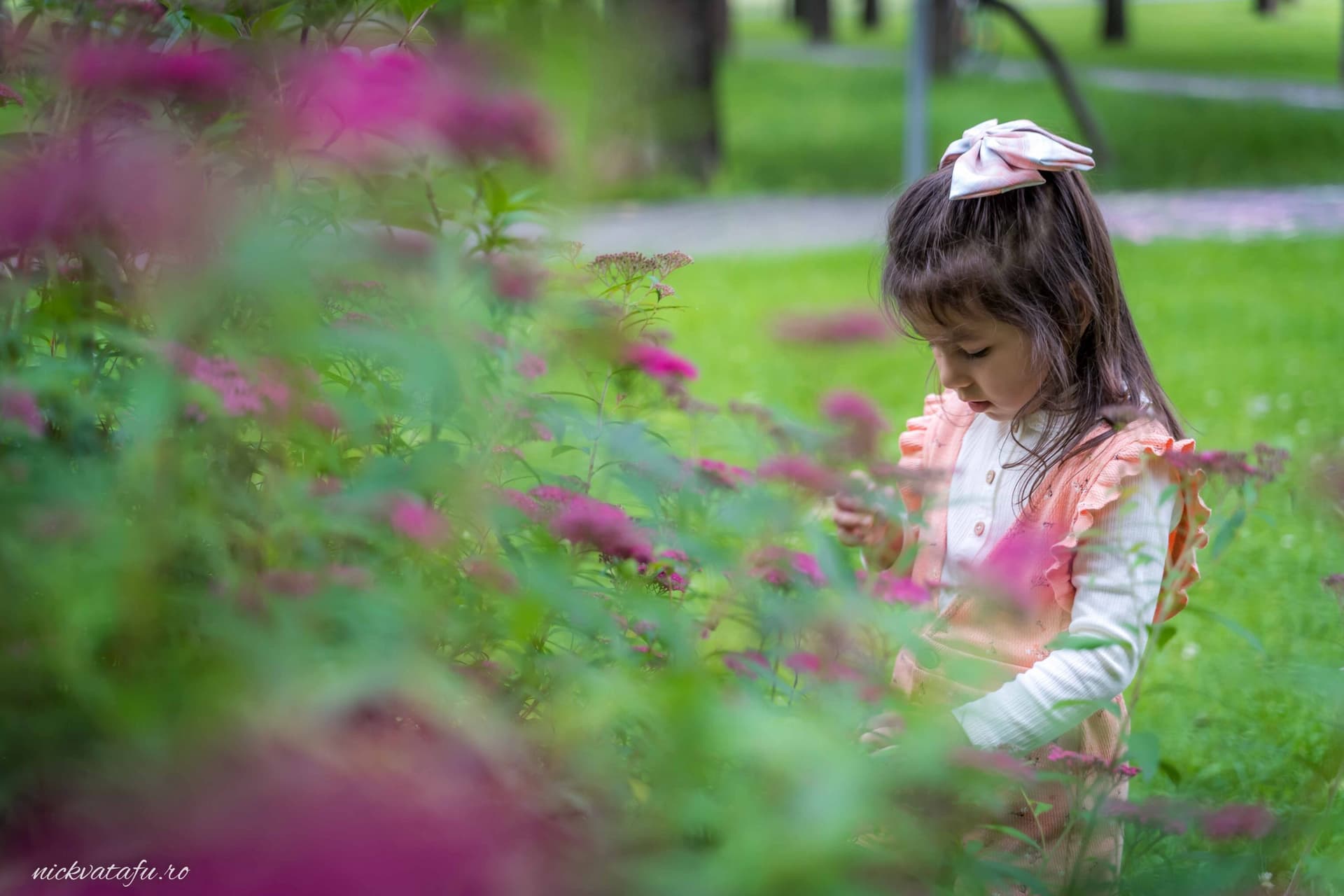 Fetiță jucându-se printre flori colorate, surprinsă în moment de bucurie, fotografie de botez în natură.