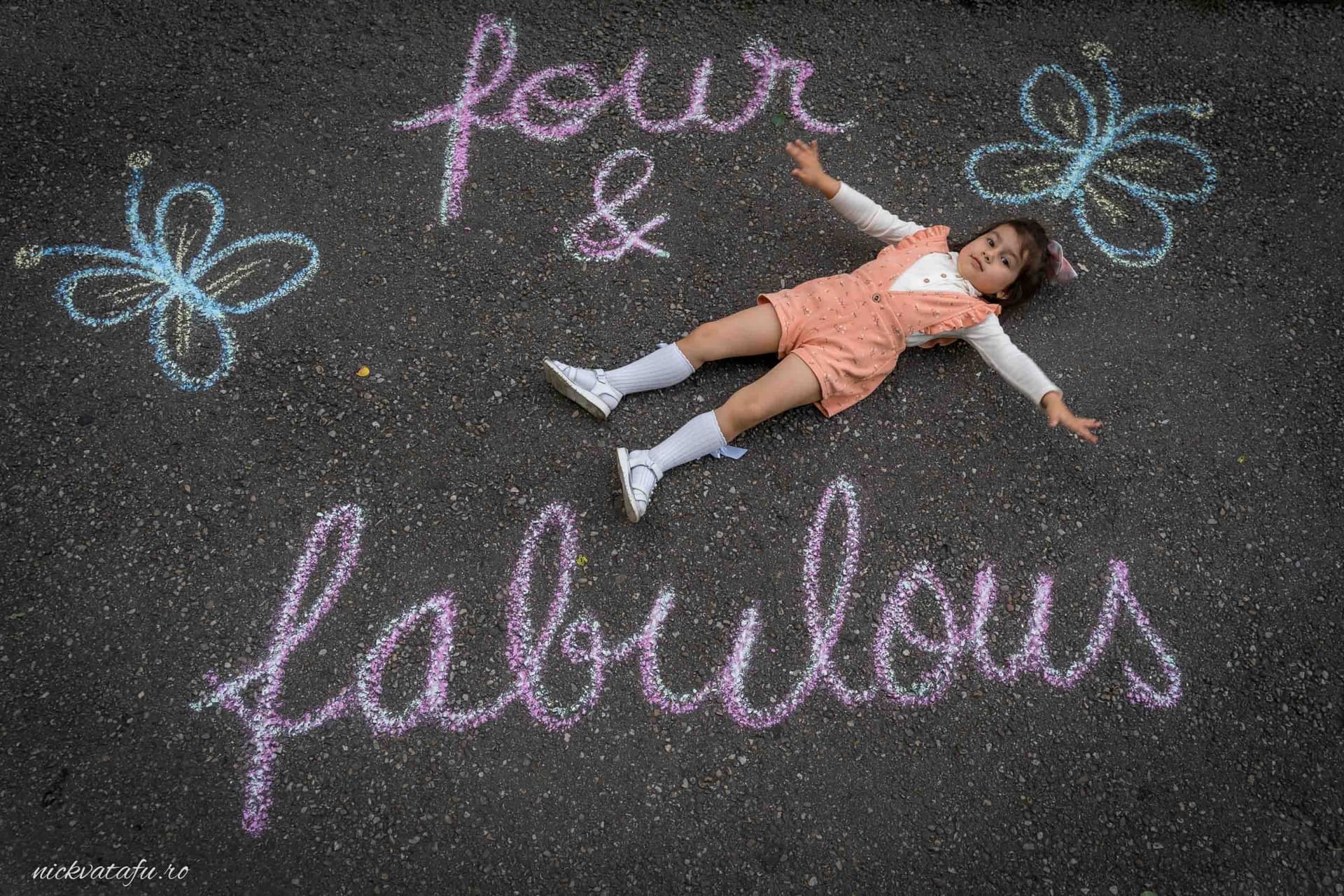 Fetiță zâmbitoare pe asfalt, înconjurată de scris cu cretă „four & fabulous”, plină de emoție și bucurie.