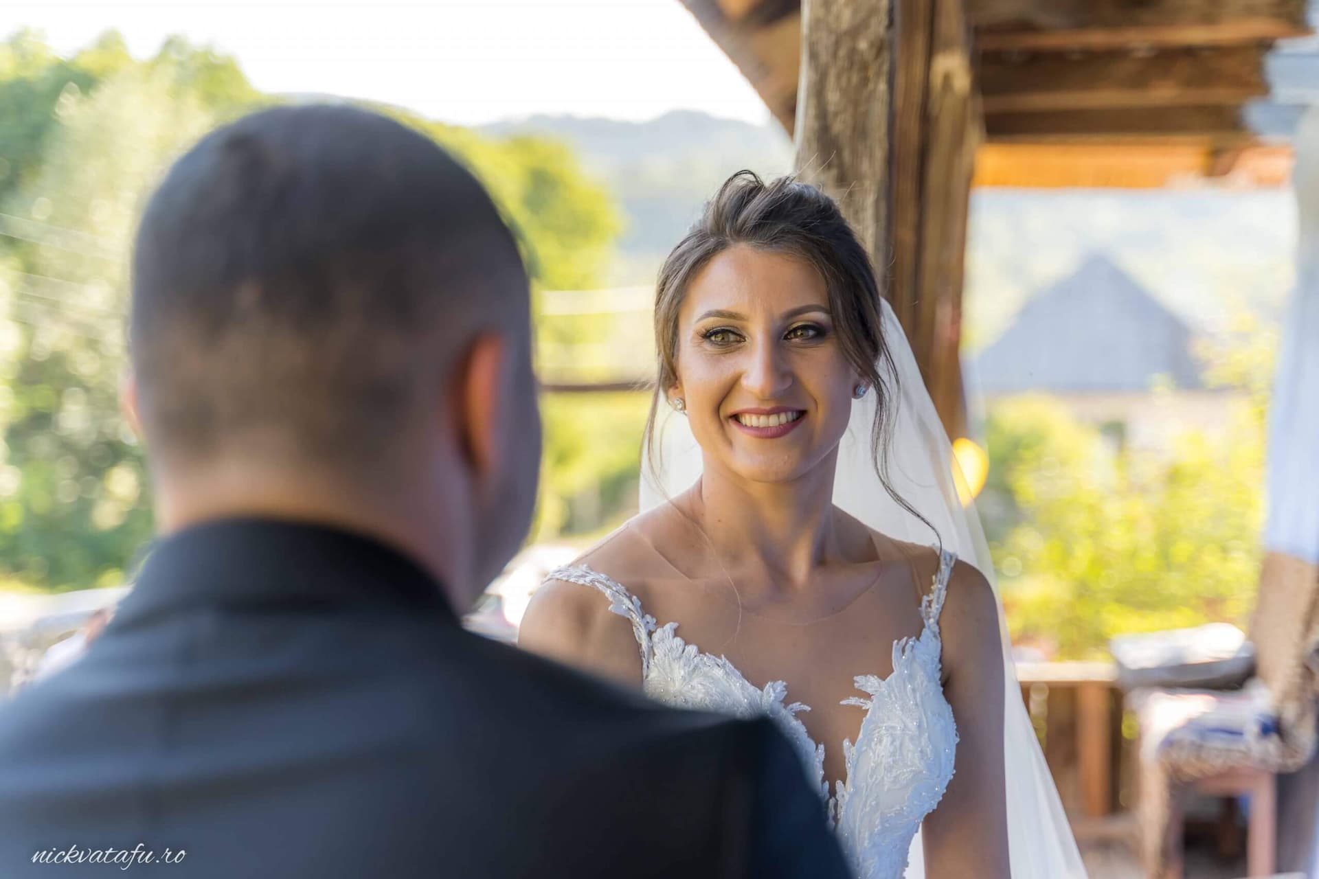 Mireasă zâmbitoare în fața mirelui, emoție și iubire în aer, fotografie de nuntă într-o locație pitorească.