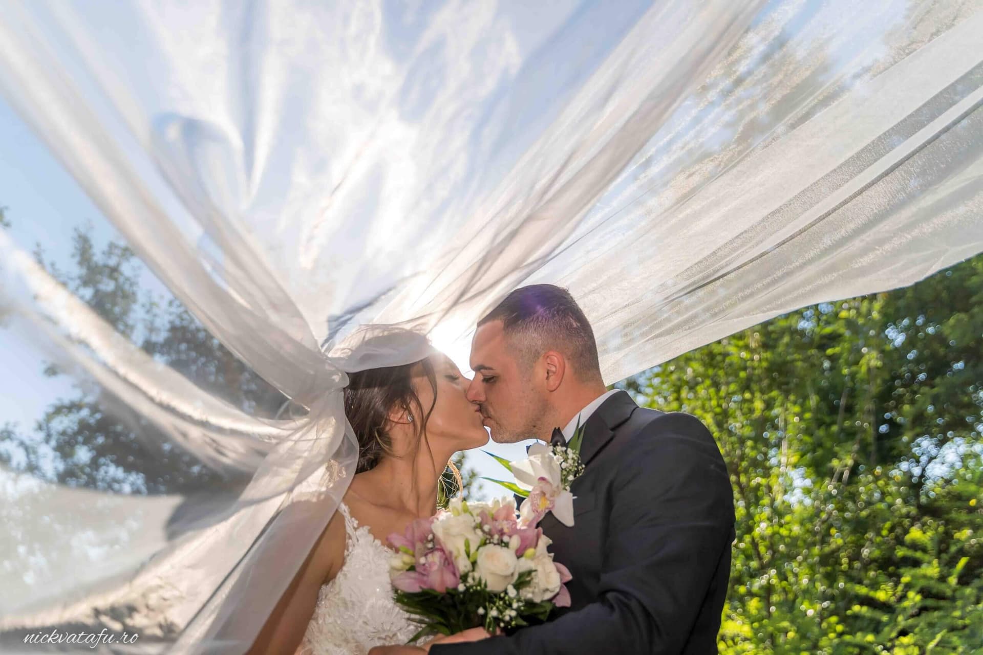 Mire și mireasă sărutându-se sub voal, emoție intensă într-o fotografie de nuntă plină de romantism.