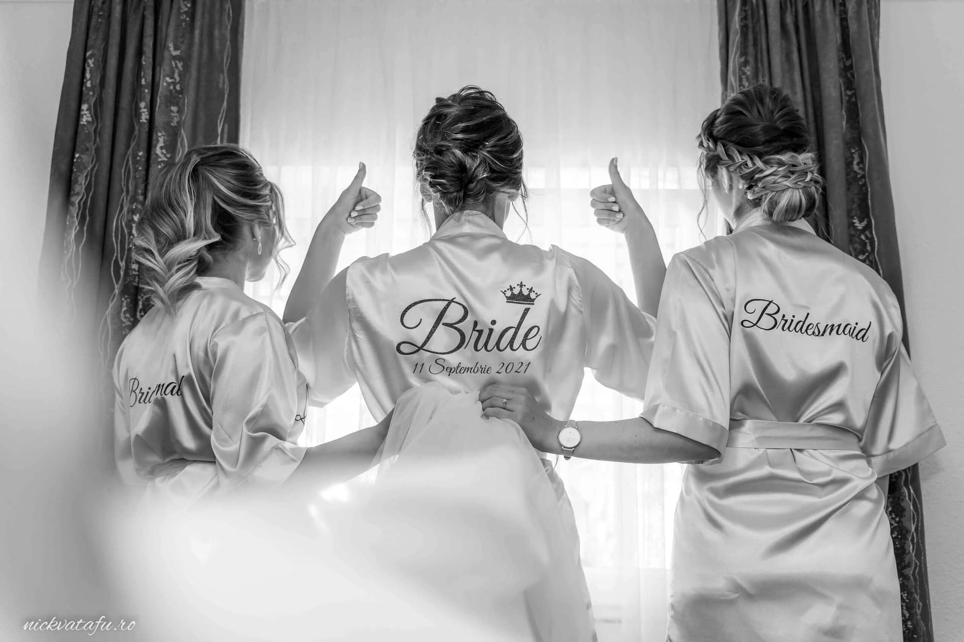 Mireasa și domnișoarele de onoare îmbrăcate în halate, zâmbind și arătând semnul „bine” înainte de nuntă.