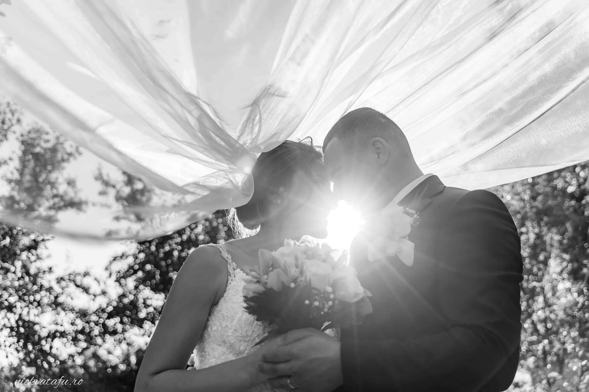 Mire și mireasă se sărută sub un drapaj elegant, emanând emoție și iubire în fotografia de nuntă.