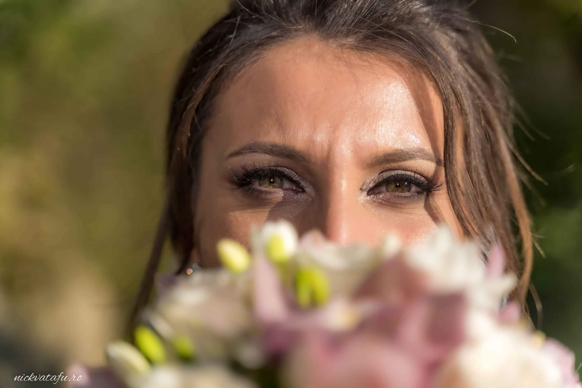 Ochii unei mirese plini de emoție, în spatele unui buchet de flori delicate, fotografie nuntă captivantă.
