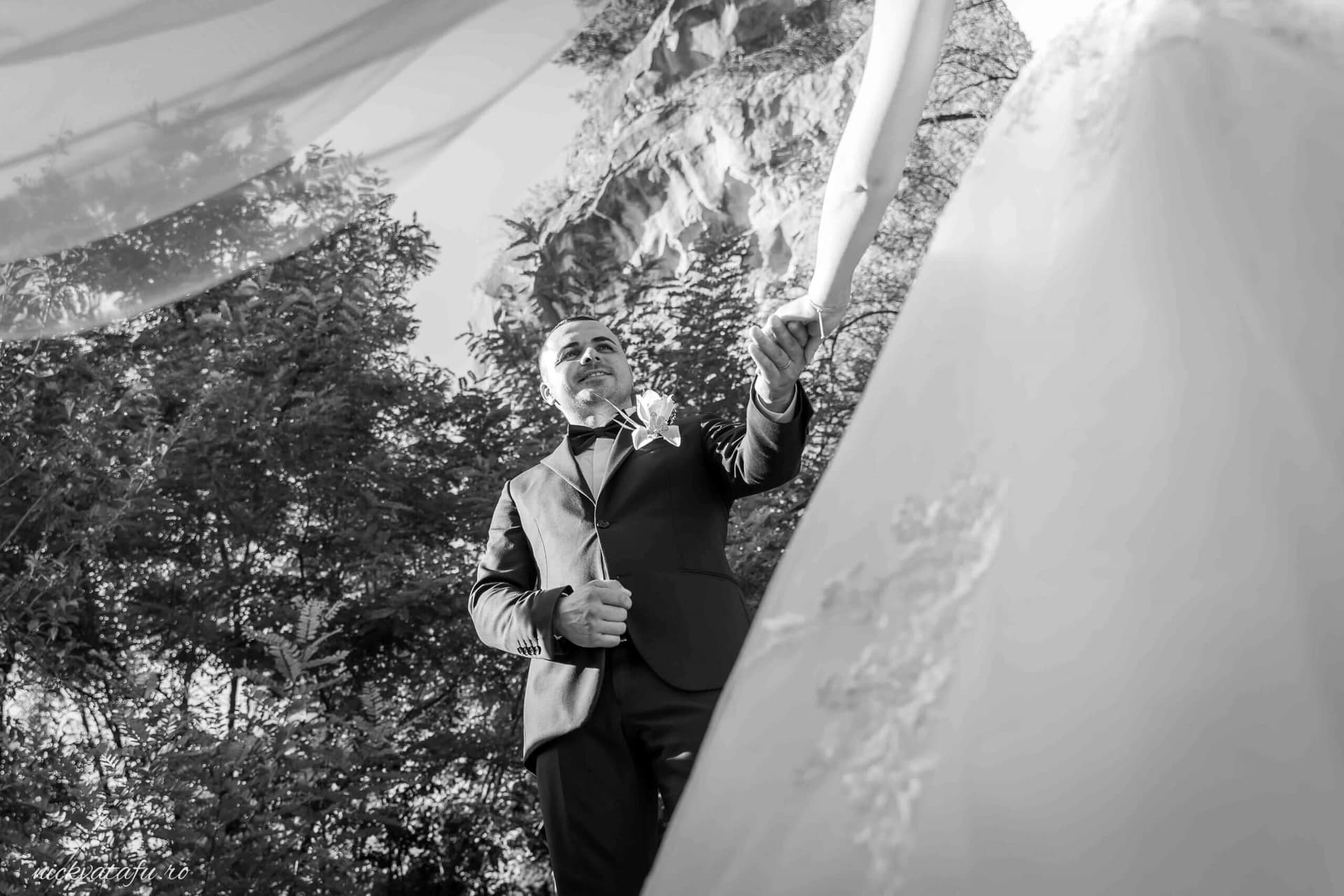 Bărbat elegant în costum, cu zâmbet larg, pregătind decorul pentru ceremonia de nuntă în aer liber.