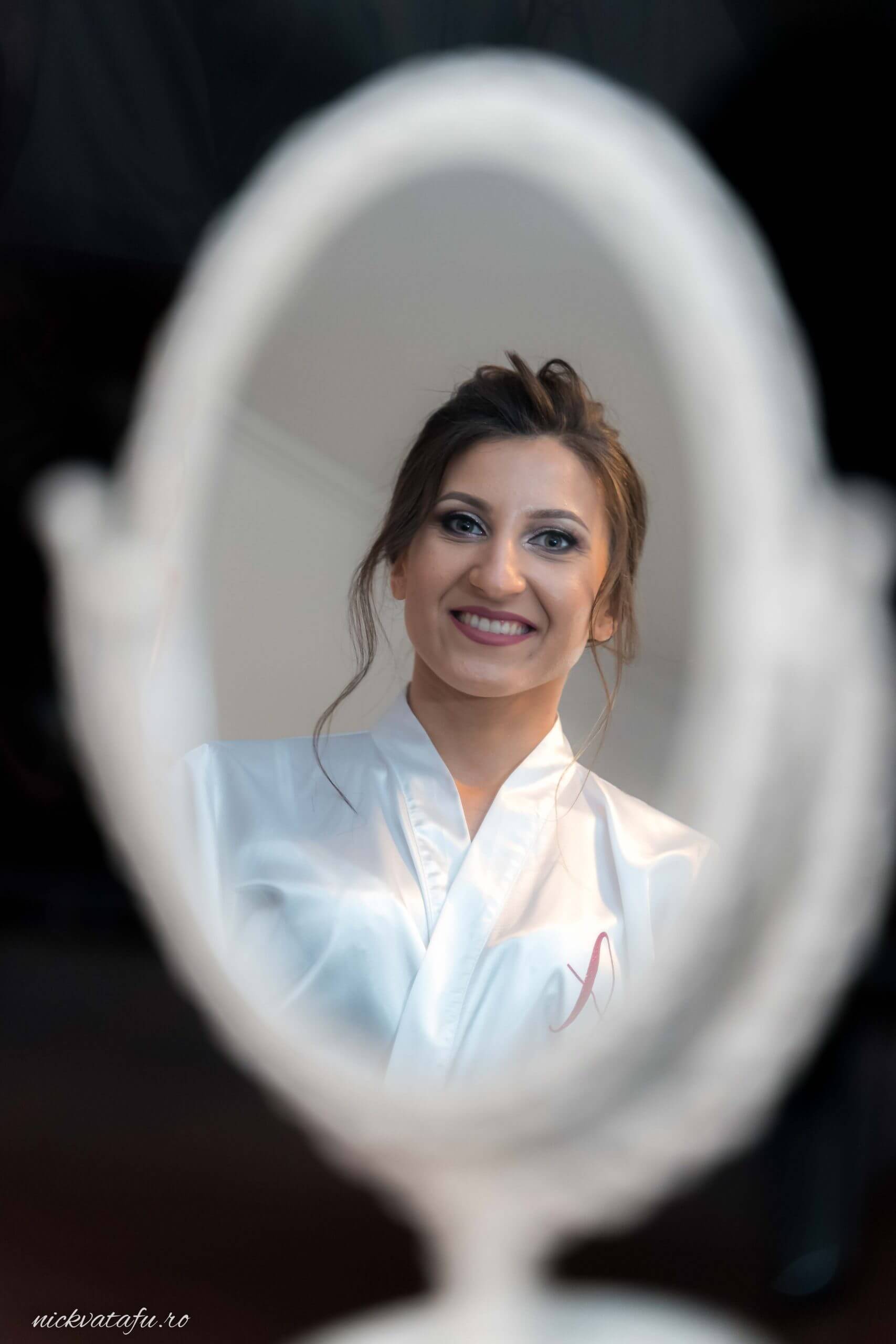 Mireasă zâmbitoare, admirându-se în oglindă, pregătiri pentru o fotografie de nuntă plină de emoție.