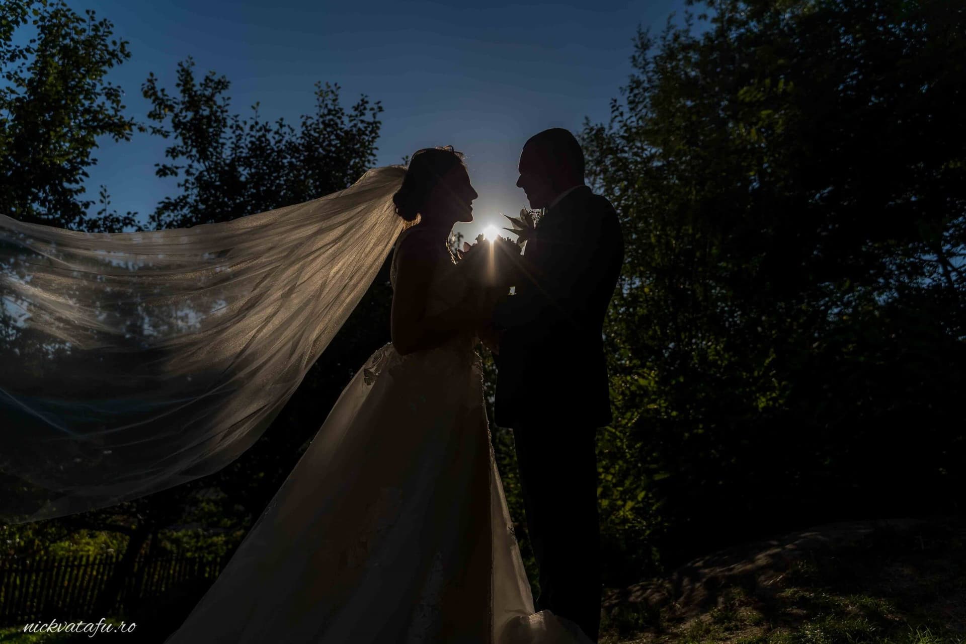 Mire și mireasă în lumina soarelui, cu voalul fluturând, fotografie de nuntă plină de emoție și romantism.