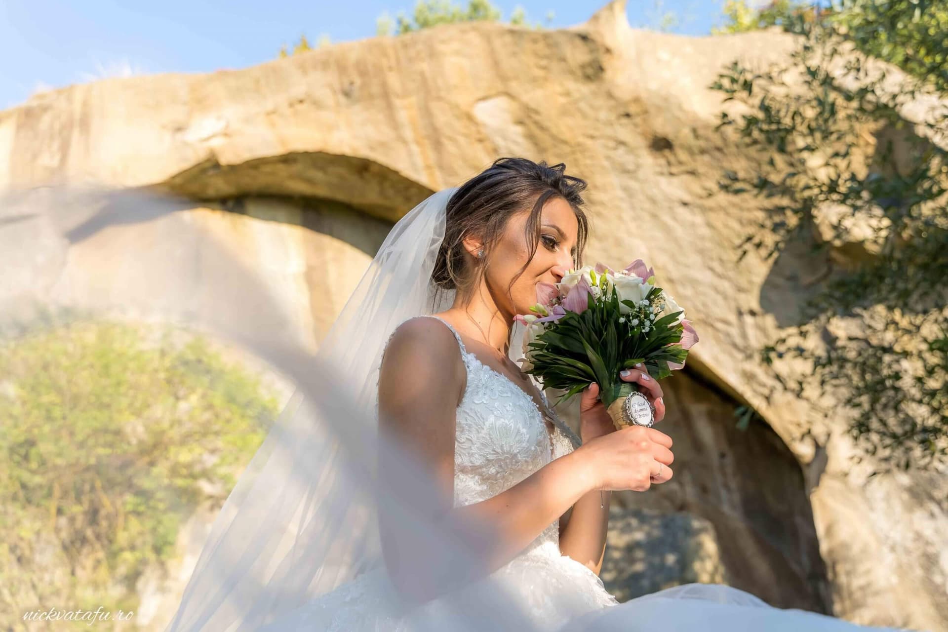 Mireasă zâmbitoare cu buchet de flori, într-un cadru natural, fotografie de nuntă plină de emoție.