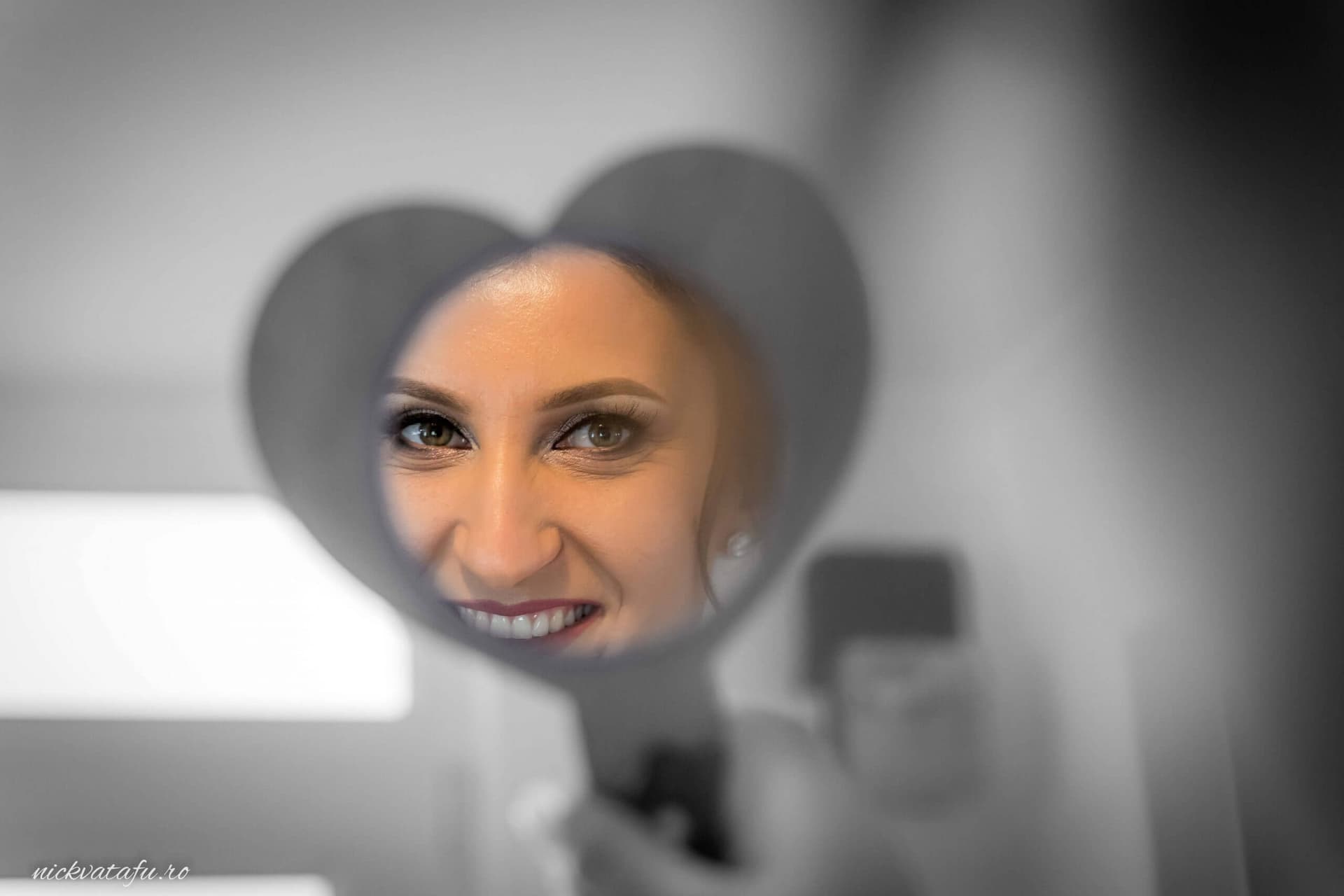 Reflecția unei mirese zâmbitoare într-o oglindă în formă de inimă, plină de emoție și bucurie.