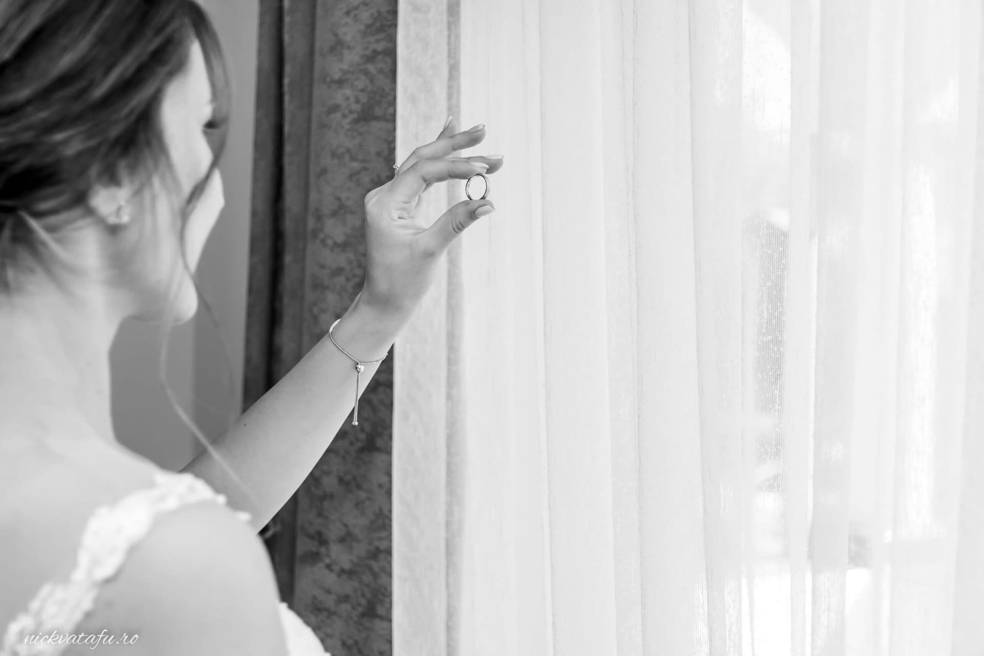 Mireasă contemplând cu emoție lumina filtrată prin perdele, fotografie de nuntă elegantă.