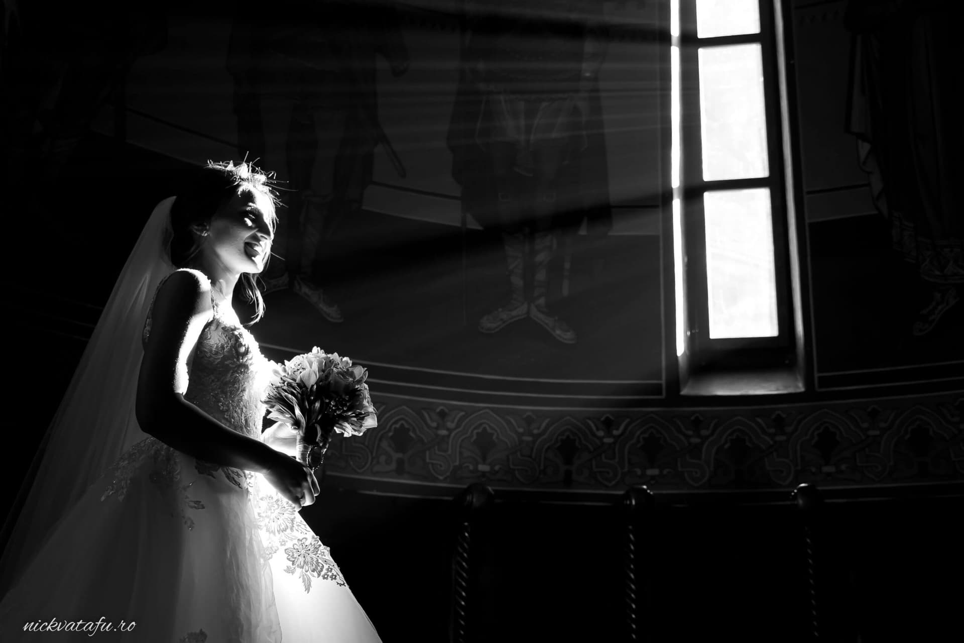 Mireasă elegantă, contemplând emoționată la fereastră, fotografie de nuntă în tonuri de alb și negru.