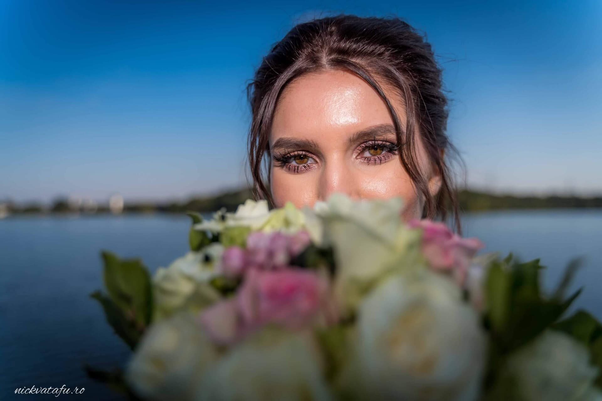 Mireasă zâmbitoare, cu buchet de flori în față, captivând privirile într-o fotografie de nuntă la apă.