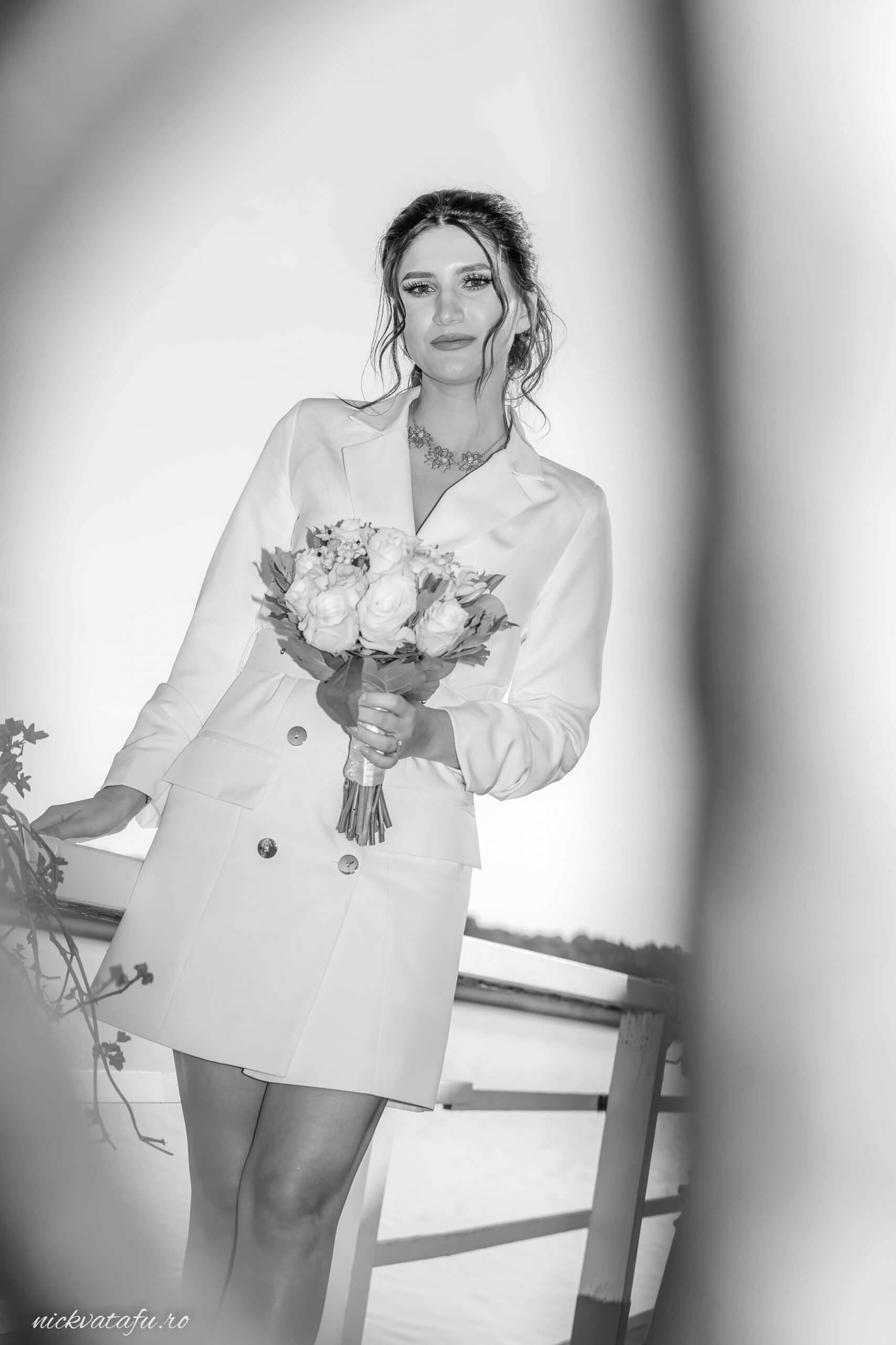Mireasă elegantă, cu buchet de flori, surprinsă într-un moment de reflecție, fotografie nuntă în alb și negru.