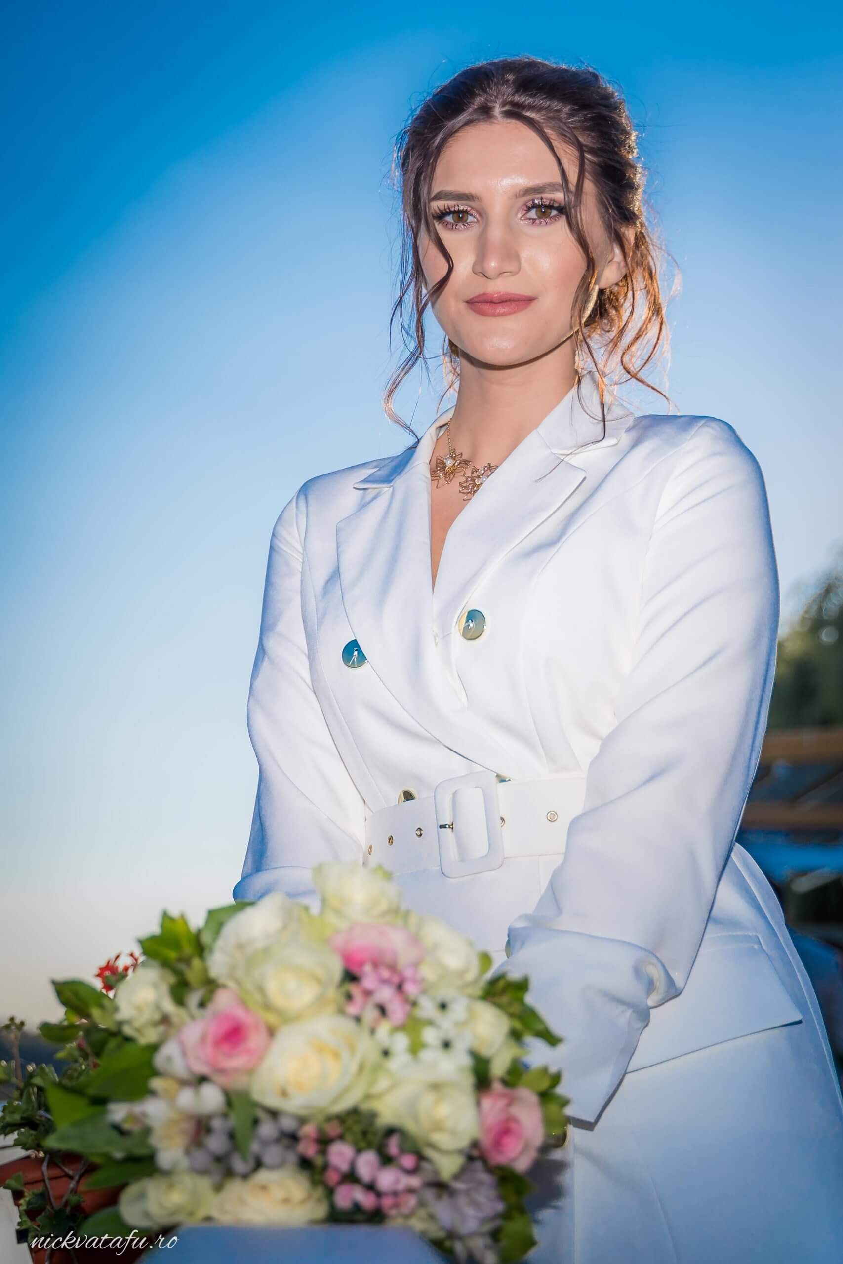 Mireasă zâmbitoare cu buchet de flori, în lumina blândă a serii, perfectă pentru o fotografie de nuntă elegantă.