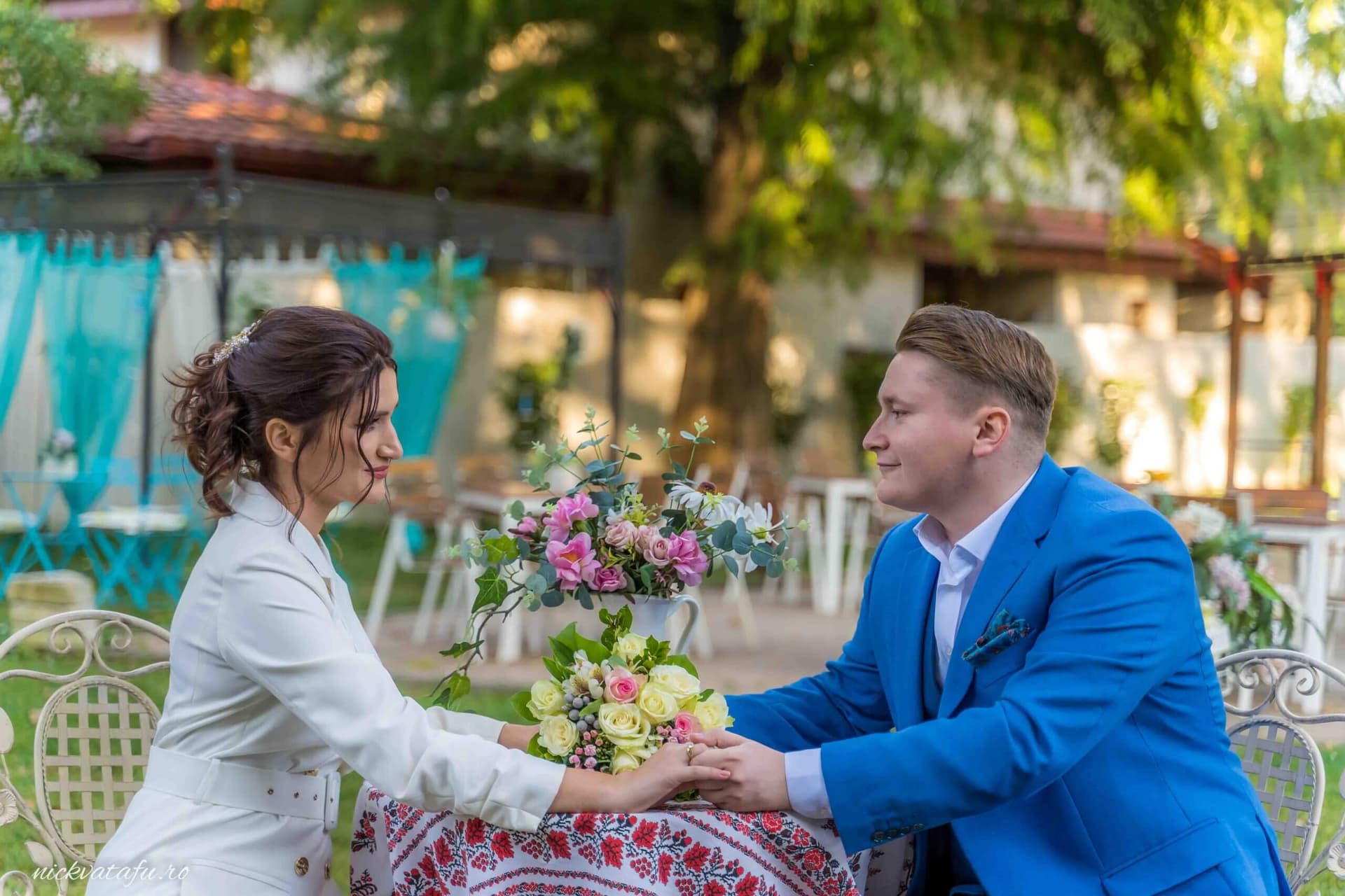 Mire și mireasă, emoționați, la o masă cu flori, într-un cadru elegant de nuntă.