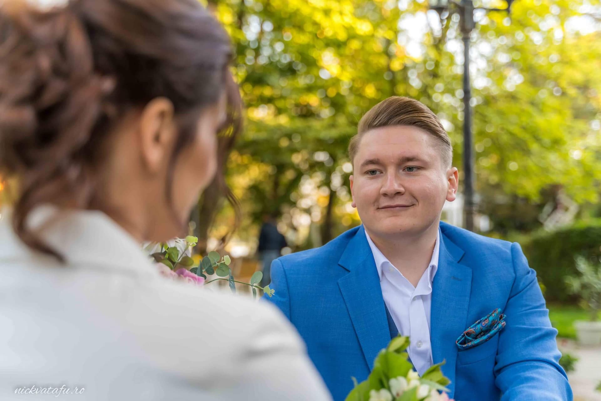 Mire în costum albastru zâmbind emoționat la întâlnirea cu mireasa, într-un parc plin de verdeață.