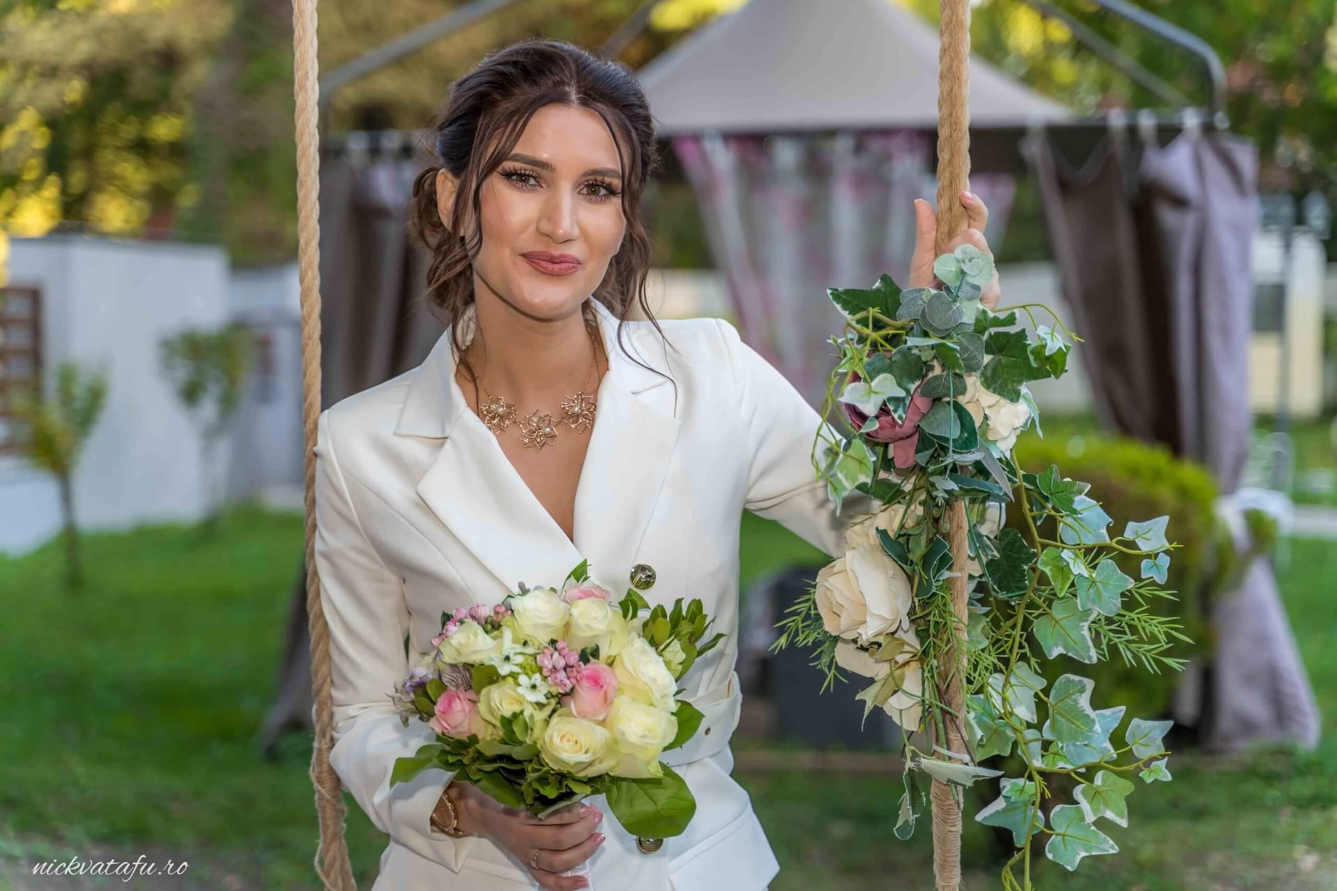 Mireasă zâmbitoare, cu buchet de flori, stând pe leagăn într-o grădină, detalii elegante de nuntă.