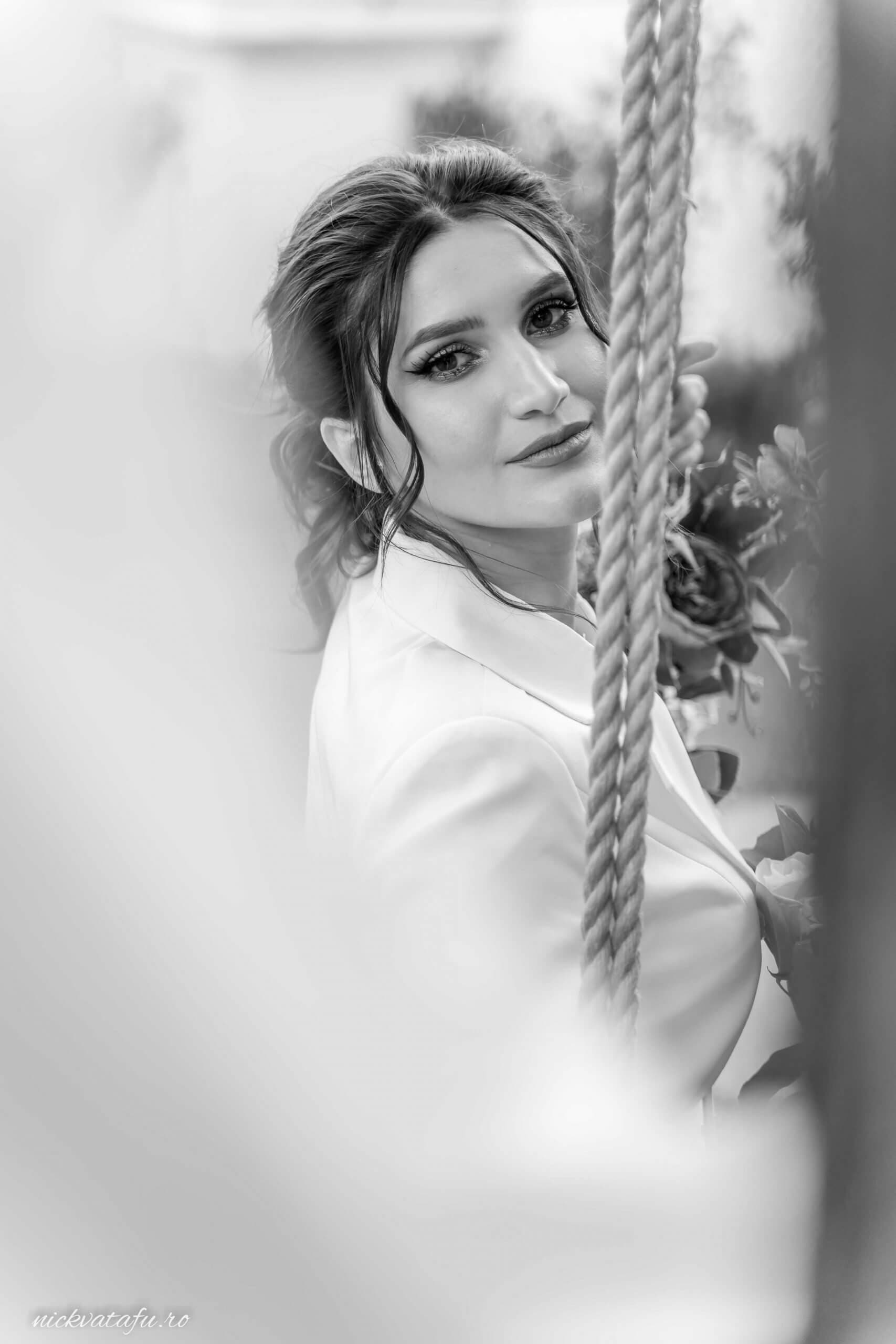 Mireasă zâmbitoare pe o leagăn, capturând emoția unei zile de nuntă unice, fotografie elegantă în alb și negru.