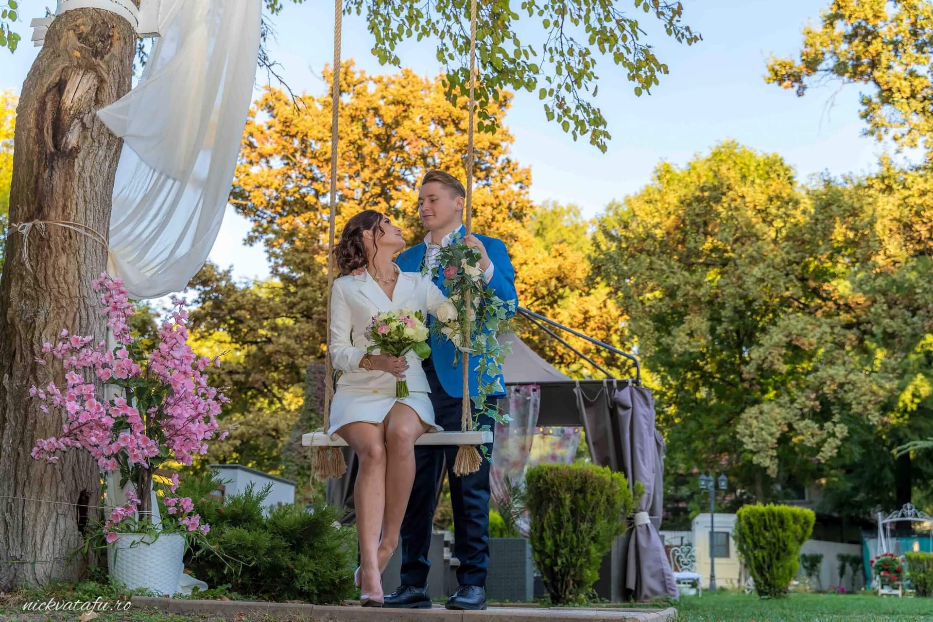 Mire și mireasă zâmbind pe o leagăn în grădină, fotografie de nuntă plină de emoție și romantism.