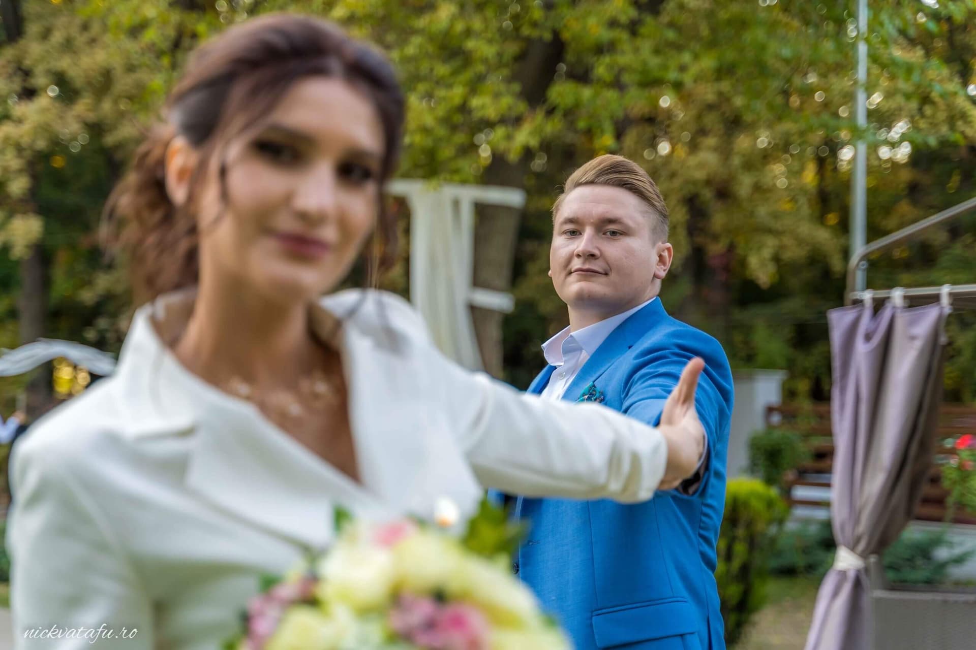 Mireasă zâmbitoare cu buchet în mână, privindu-l pe mire, într-un cadru natural plin de emoție.