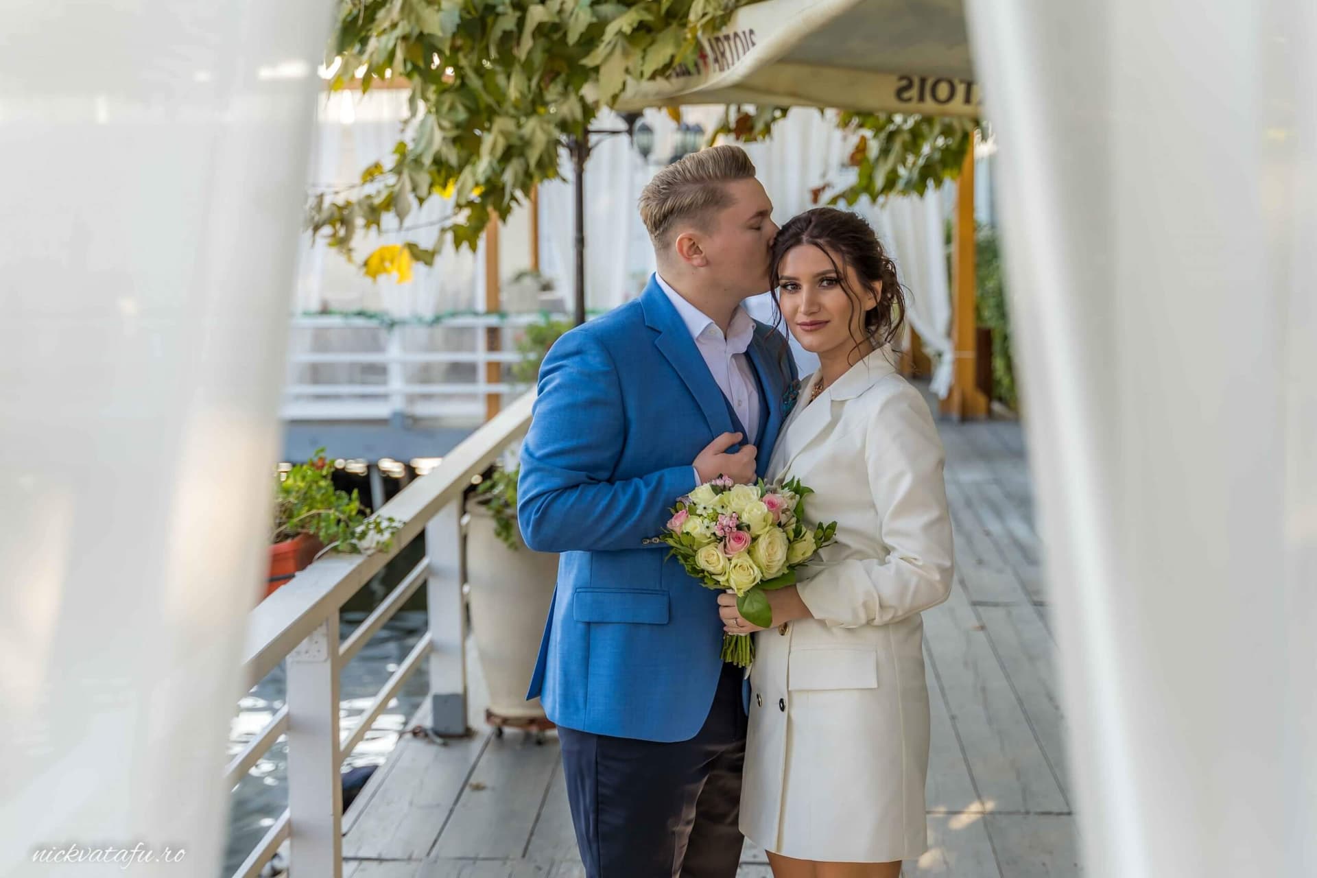 Mire și mireasă zâmbind pe un pod, cu un buchet de flori, fotografie elegantă de nuntă plină de emoție.