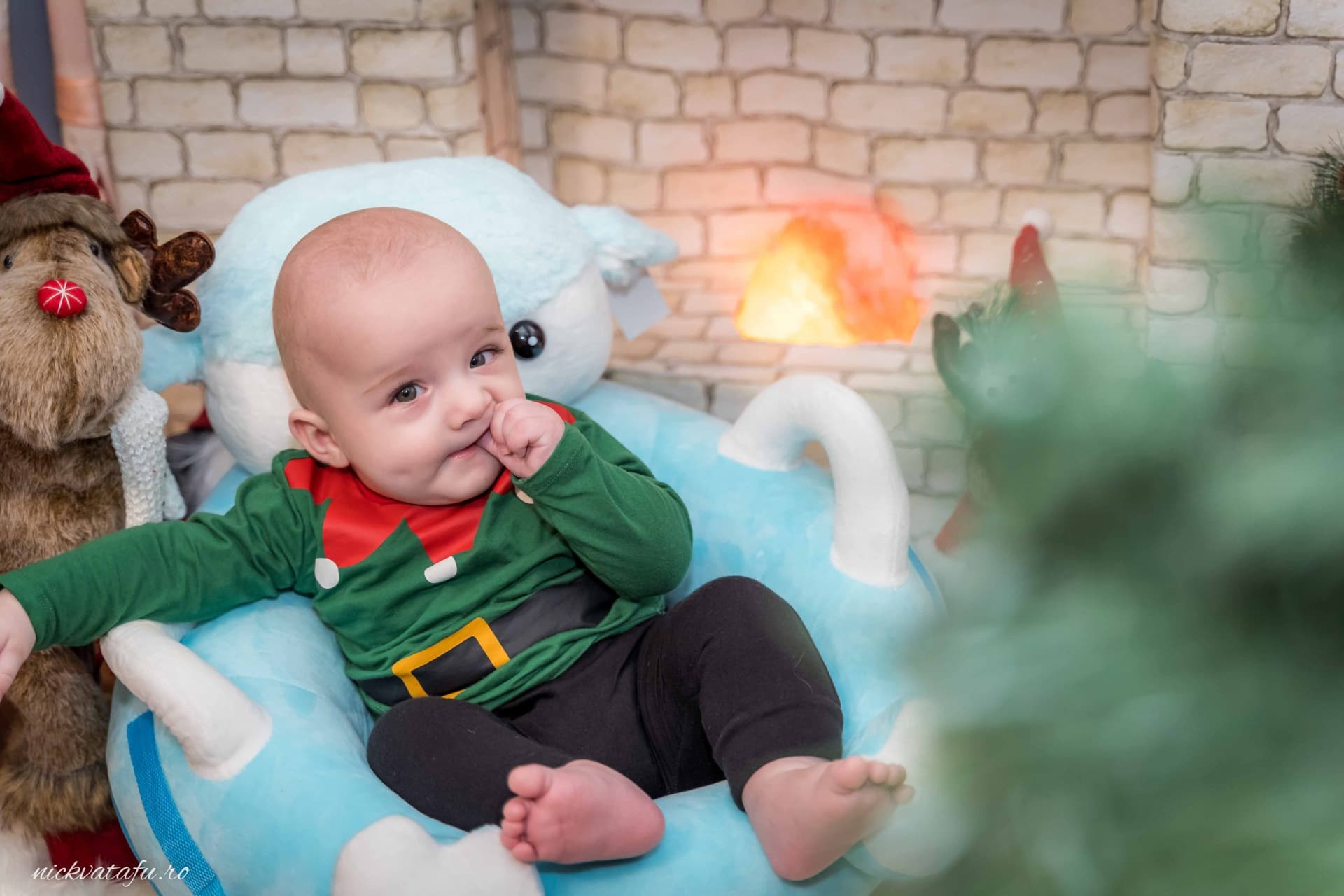 Bebeluș zâmbitor, îmbrăcat în costum de elf, relaxându-se într-un decor festiv, fotografie de botez plină de emoție.