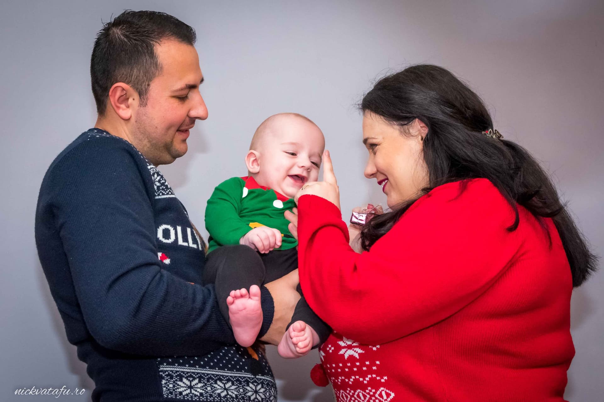 Părinți fericiți își îmbrățișează copilul zâmbitor, capturând emoția unui moment de familie special.