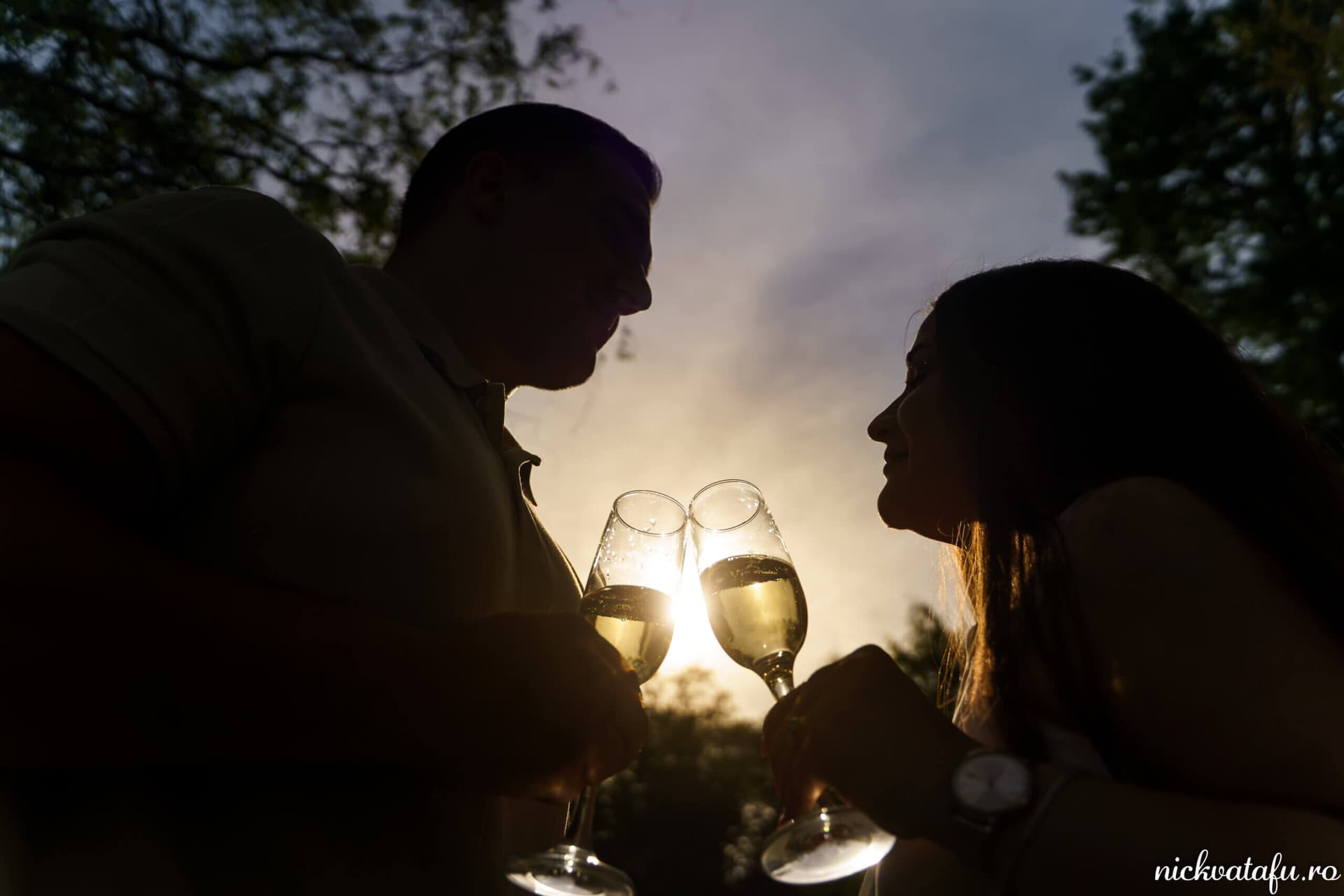 Mire și mireasă ciocnind paharele în lumina apusului, fotografie de nuntă plină de emoție și intimitate.