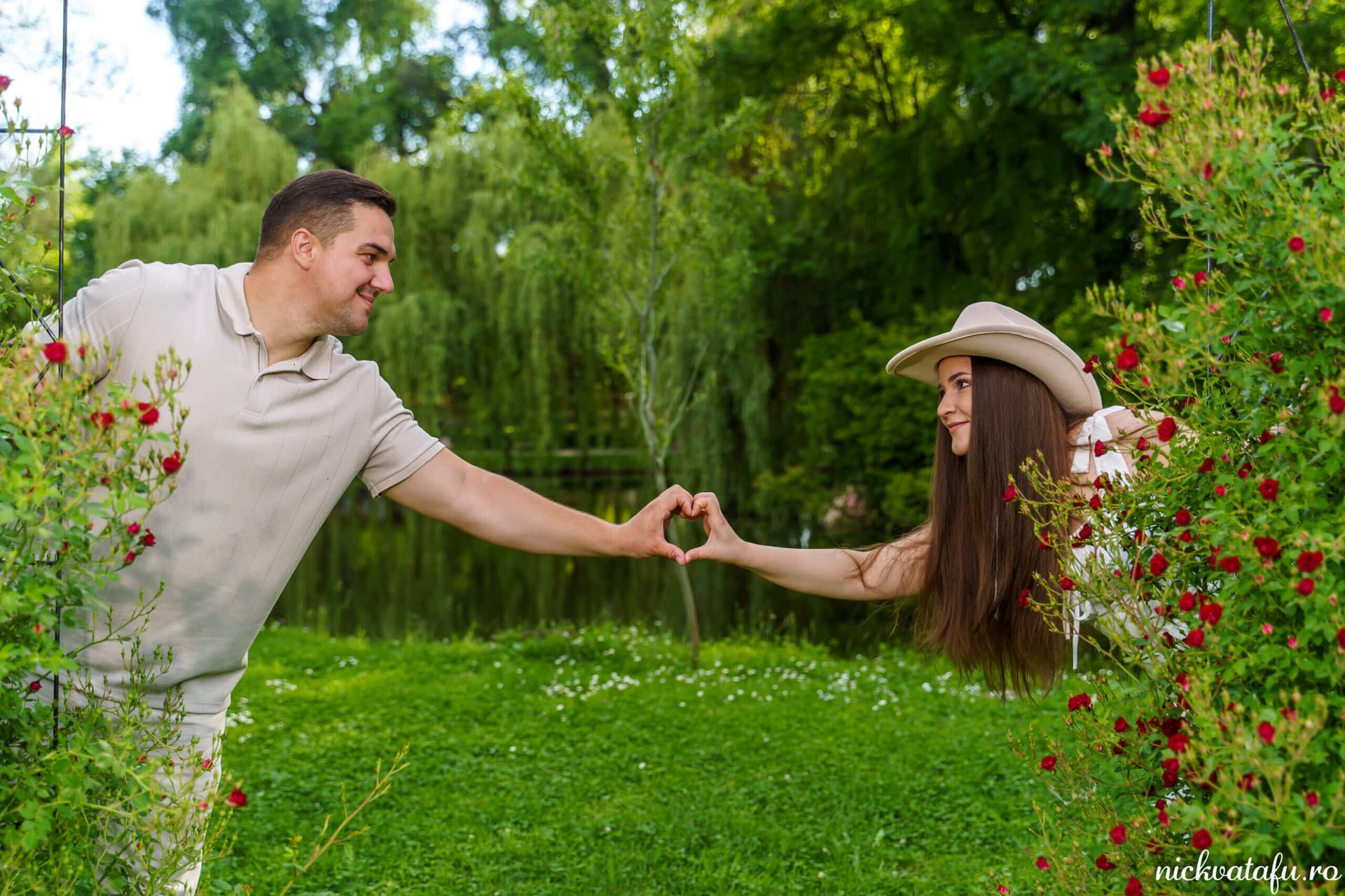 Mire și mireasă formează un inimioară cu mâinile, înconjurați de flori, într-un peisaj romantic de nuntă.