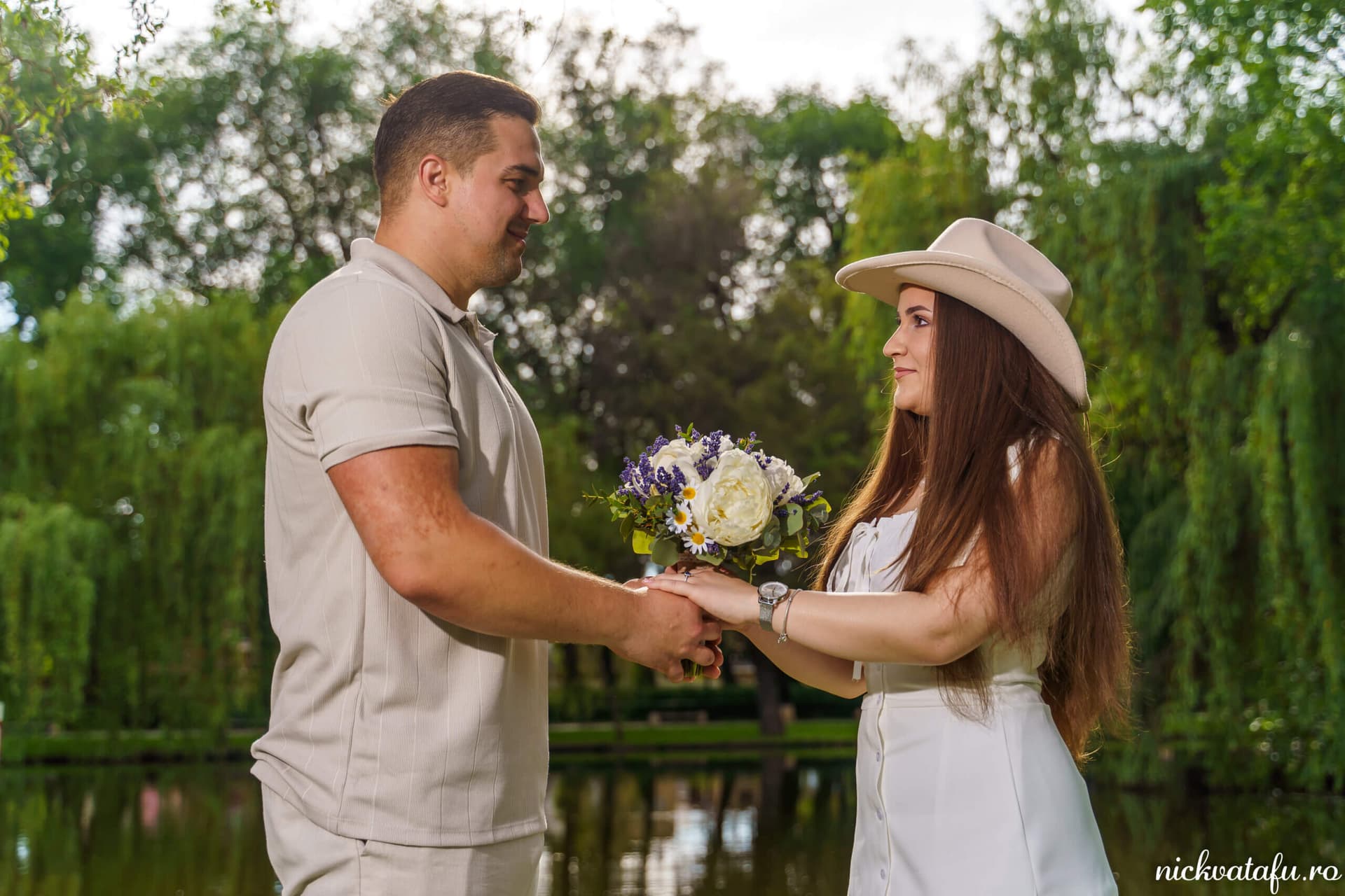 Mire și mireasă își țin mâinile într-un moment plin de emoție, în parc, cu flori de nuntă în brațe.